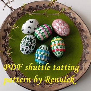 May include: Six colorful Easter eggs decorated with white lace tatting. The eggs are on a green plate with a brown rim. The text "PDF shuttle tatting pattern by Renulek" is at the bottom of the image.