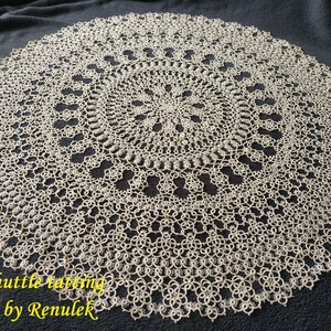 Pode incluir: Um grande tapete de crochê circular branco com um padrão detalhado. O tapete é feito com um design delicado e intrincado e tem um centro ligeiramente elevado. O texto "PDF shuttle tatting pattern by Renulek" é visível no canto inferior direito da imagem.