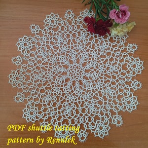 May include: A white, circular doily with an intricate, lace-like pattern. The doily is made using the shuttle tatting technique. The image includes the text "PDF shuttle tatting pattern by Renulek" and a sprig of flowers.
