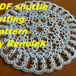 May include: White crocheted doily with a delicate pattern. The doily is round and has a center circle with a smaller circle inside. The doily is surrounded by a border of smaller circles. The text "PDF shuttle tatting pattern by Renulek" is written in yellow letters on top of the doily.