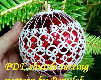 May include: A red Christmas ornament covered in white crocheted lace. The ornament is being held in a hand. The text "PDF shuttle tatting pattern by Renulek" is visible at the bottom of the image.