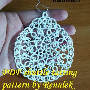 May include: White crocheted lace doily with a circular design. The doily is held in a hand and the text "PDF shuttle tatting pattern by Renulek" is visible below the doily.