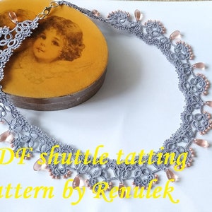 May include: A gray crocheted necklace with pink beads. The necklace is on a white surface and a vintage-style box with a picture of a child on the lid. The text "PDF shuttle tatting pattern by Renulek" is below the necklace.