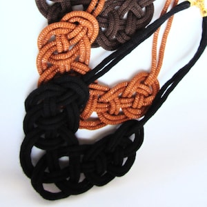 May include: Three knotted rope necklaces in brown, orange, and black. The necklaces are made of thick rope and have a simple, elegant design.