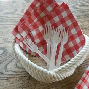 May include: A white rope basket filled with red and white checkered napkins and white plastic forks.