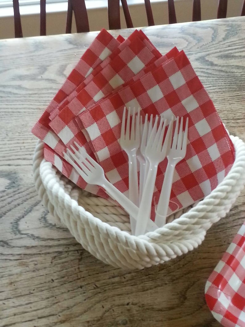 May include: A white rope basket filled with red and white checkered napkins and white plastic forks.