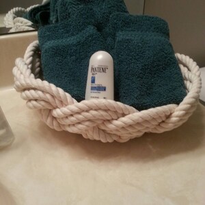 May include: A white rope basket containing a teal blue towel and a small white bottle of Pantene Pro-V conditioner.