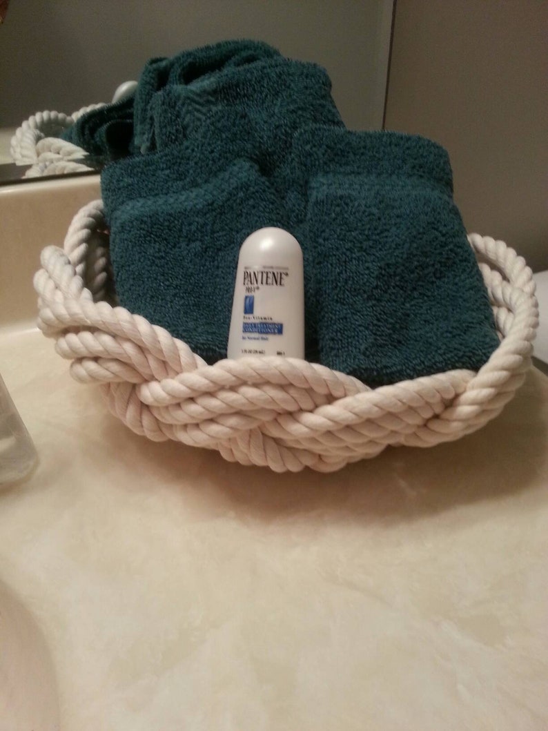 May include: A white rope basket containing a teal blue towel and a small white bottle of Pantene Pro-V conditioner.