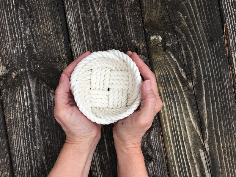 May include: A white rope basket with a woven pattern, held in two hands.