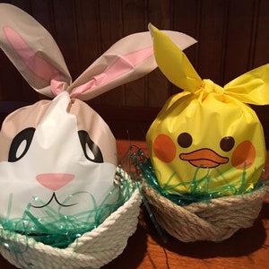May include: Two Easter baskets filled with green grass and decorated with a bunny and a duck. The bunny basket is white with pink ears and a brown face. The duck basket is yellow with a black beak and eyes.