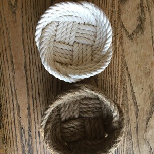May include: Two woven rope baskets, one white and one brown, on a wooden surface.