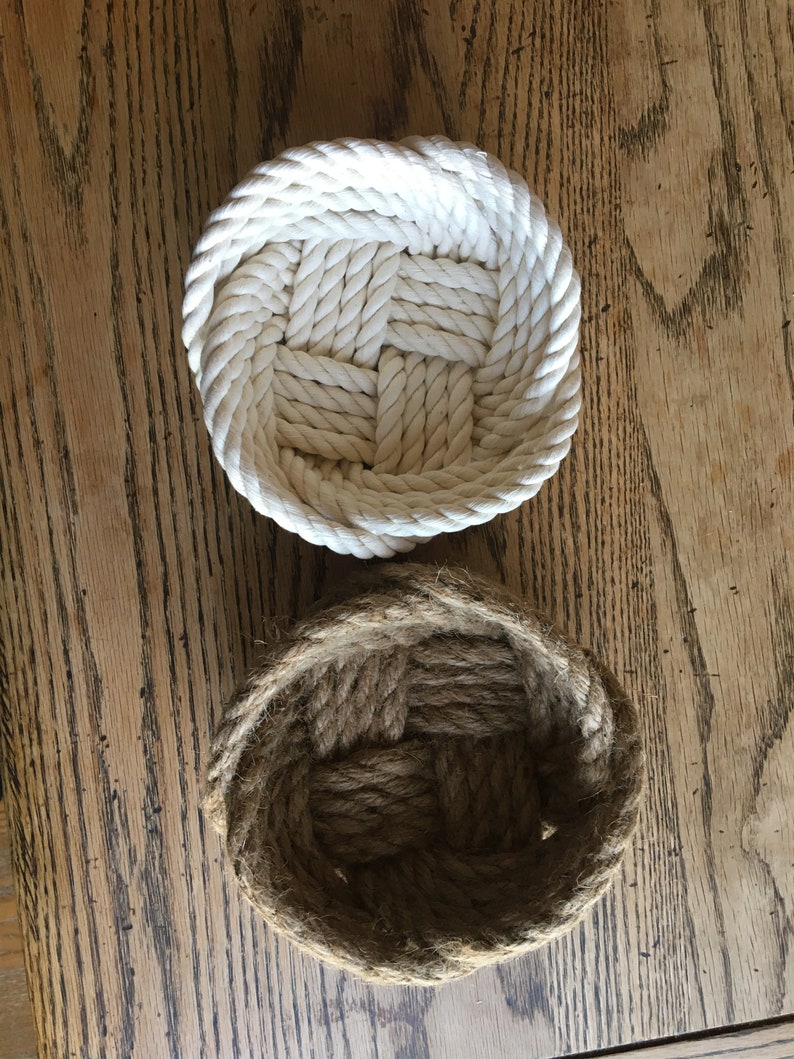 May include: Two woven rope baskets, one white and one brown, on a wooden surface.