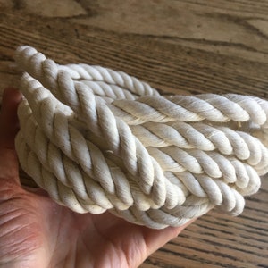 May include: A thick, white cotton rope coiled into a circle. The rope is soft and natural looking.