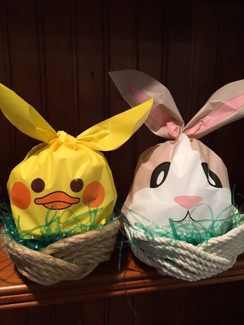 May include: Two Easter baskets, one shaped like a yellow duck and the other shaped like a white bunny, are filled with green grass and placed on a wooden shelf.