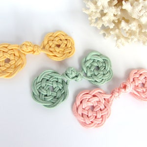 May include: Three handmade macrame rope ornaments in yellow, green, and pink. Each ornament is a circle with a smaller circle in the center. The ornaments are connected by a knot.