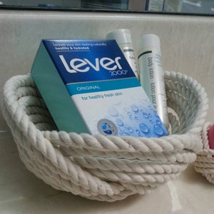 May include: A white rope basket filled with toiletries, including a bar of Lever 2000 soap, a bottle of body lotion, and a bottle of hand lotion.