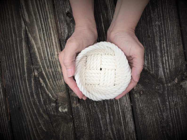 May include: A white rope coaster with a woven design, held in two hands.