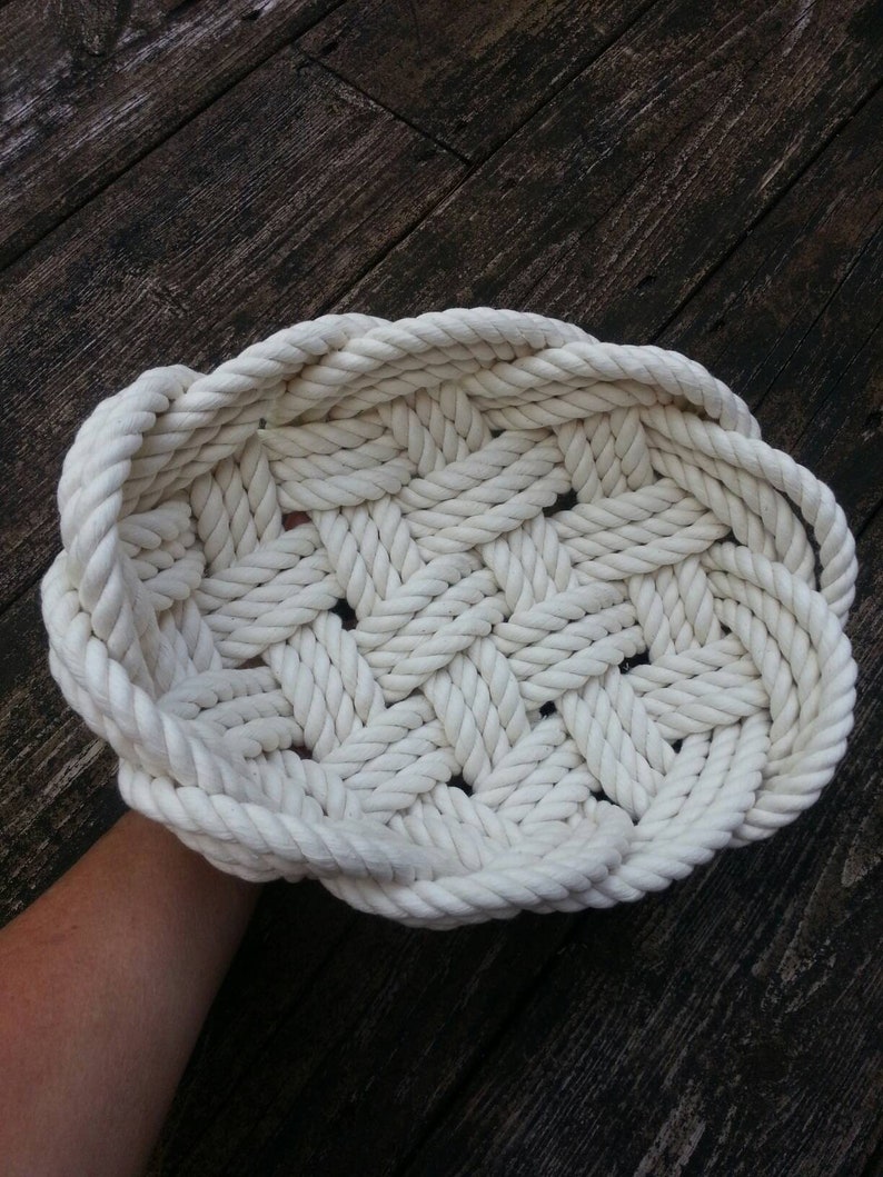 May include: A white rope basket woven in a lattice pattern. The basket is round and has a wide, flat base.