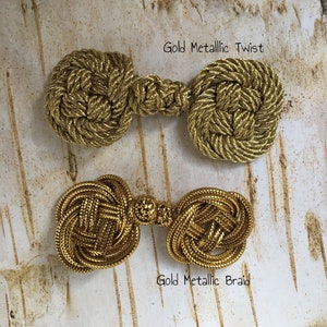 May include: Two gold metallic rope toggles. The top toggle is a twist design and the bottom toggle is a braid design. The text "Gold Metallic Twist" is above the top toggle and the text "Gold Metallic Braid" is below the bottom toggle.