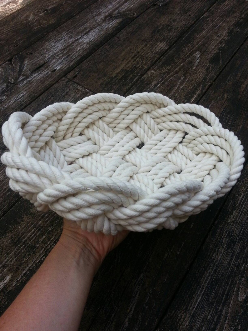 May include: A white rope basket woven into a circular shape. The basket is made of thick, white rope and has a slightly raised edge.