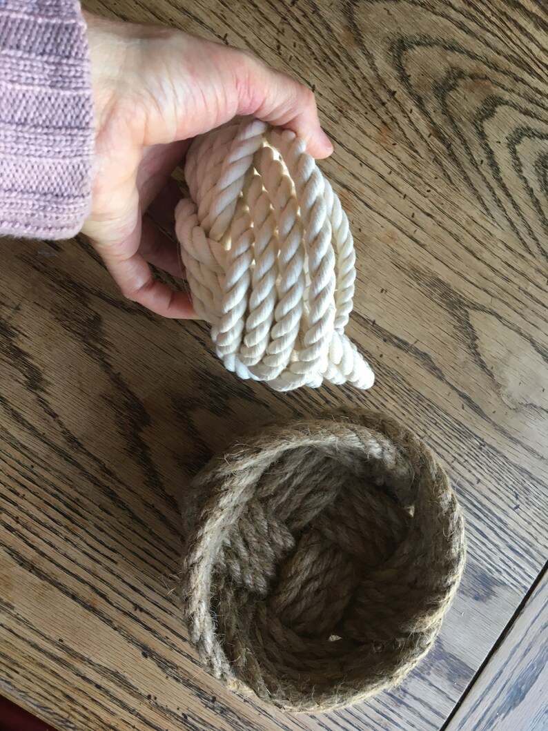 May include: Two rope baskets, one is white and the other is brown. The white rope basket is coiled up and the brown rope basket is open and ready to hold items.