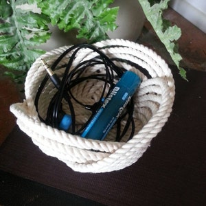 May include: A white rope basket containing a blue and white battery, black headphones, and a white cord.