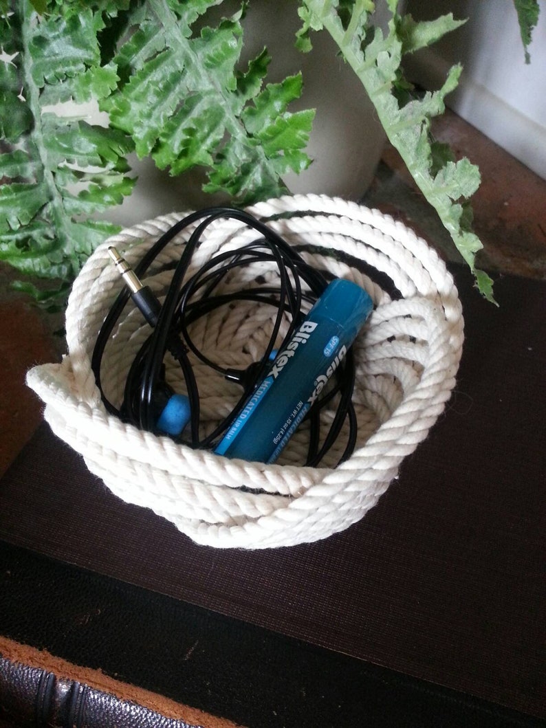 May include: A white rope basket containing a blue and white battery, black headphones, and a white cord.