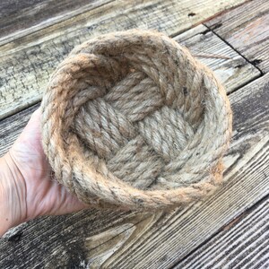 May include: A woven rope bowl made from natural jute fibre. The bowl is oval shaped and has a rustic, natural look.