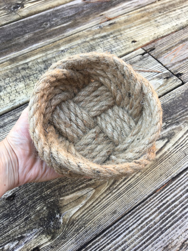 May include: A woven rope bowl made from natural jute fibre. The bowl is oval shaped and has a rustic, natural look.