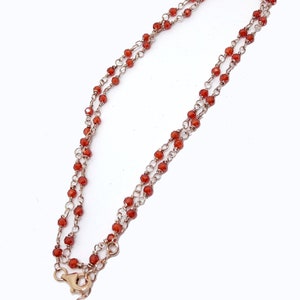 Könnte beinhalten: Eine zarte goldene Kettenkette mit zwei Reihen kleiner, roter Karneolperlen.