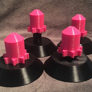 May include: Four pink and black 3D printed knobs with a star-shaped base. The knobs are on a gray surface.