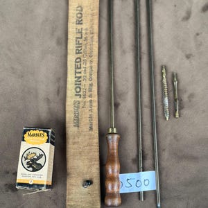 May include: A vintage Marble's Jointed Rifle Rod set. The set includes a canvas case with text, a wooden-handled rod, and several cleaning attachments. The box of Marble's cleaning patches is also included.