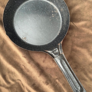 May include: A black speckled cast iron frying pan with a long black handle.