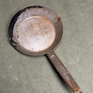 May include: A vintage cast iron skillet with a black handle. The skillet has a worn, rustic look and is marked with the text "The Lodge Manufacturing Co."