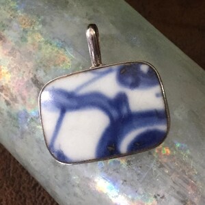 May include: A silver pendant with a rectangular blue and white porcelain tile featuring a swirling design.