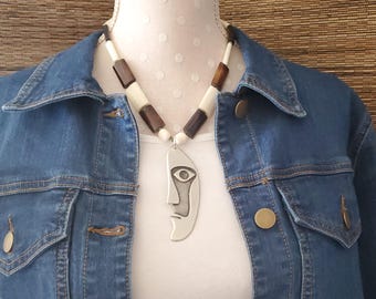 May include: A silver necklace with a face-shaped pendant and brown and white beads.