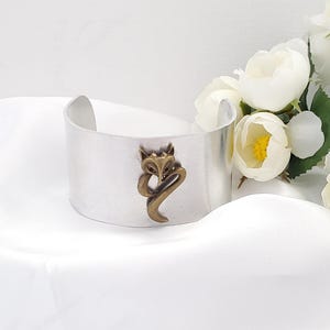 May include: Silver cuff bracelet with a fox design. The fox is made of brass and is in a crouching position.