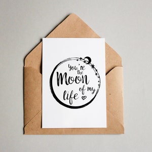 Puede incluir: Una tarjeta blanca con un c&iacute;rculo negro y el texto "You're the Moon of my life" dentro del c&iacute;rculo. La tarjeta est&aacute; en un sobre marr&oacute;n.