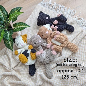 May include: Four crocheted cat plushies in different colors and patterns. The plushies are approximately 10 inches tall and are lying on a beige crocheted blanket. SIZE: (not including tail) approx. 10" (25 cm)