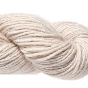 Puede incluir: Un ovillo de hilo suave de color natural. El hilo es de lana y es perfecto para tejer o hacer ganchillo.