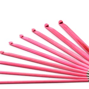 Può includere: Un set di nove uncinetti rosa con punte argentate. Gli uncinetti sono disposti a ventaglio, con l'uncinetto più grande in alto e quello più piccolo in basso.