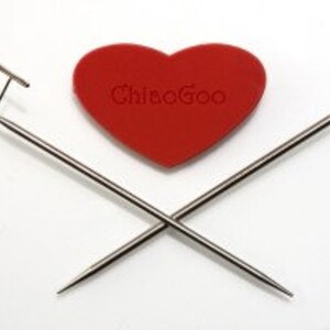 May include: Two silver knitting needles crossed over each other with a red heart-shaped knitting needle case in the center. The case has the text "Chiaogoo" printed on it.
