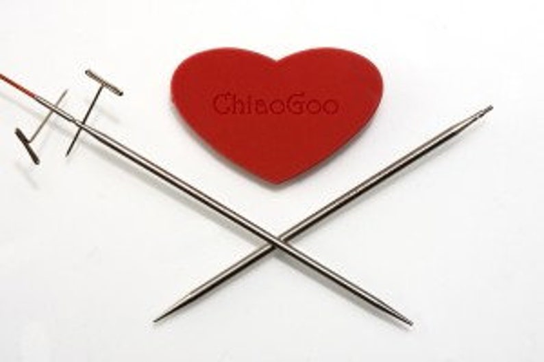May include: Two silver knitting needles crossed over each other with a red heart-shaped knitting needle case in the center. The case has the text "Chiaogoo" printed on it.