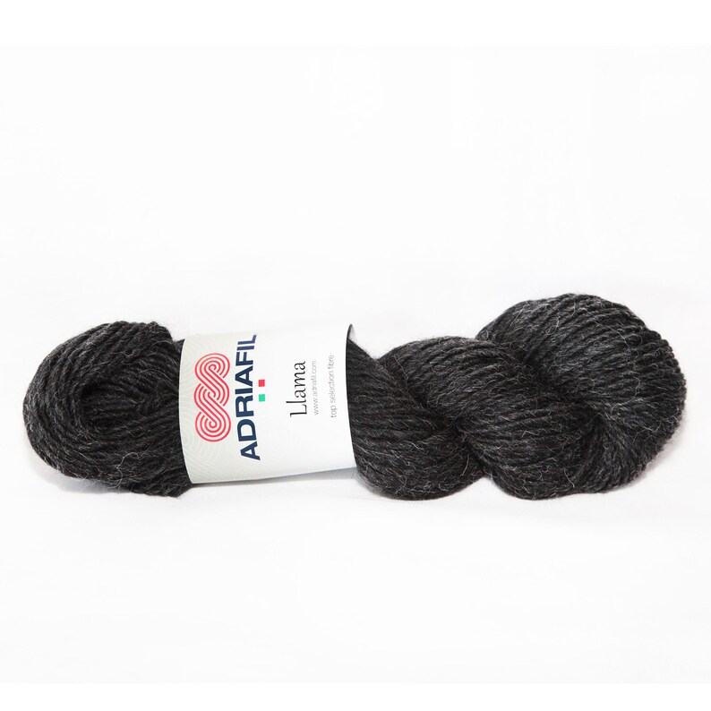 Puede incluir: Un ovillo de lana de llama gris oscuro de Adriafil. La etiqueta dice "Llama" y "100% fibras de alpaca puras".