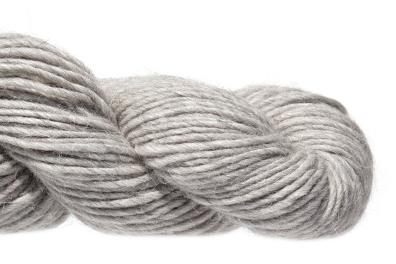 Puede incluir: Un ovillo de hilo gris claro, hecho de una mezcla de lana y alpaca.