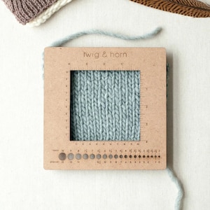 May include: A wooden gauge with a grid for measuring knit fabric, labeled "twig & horn". The gauge has a ruler in inches and centimeters, and a needle size guide in US and metric sizes.