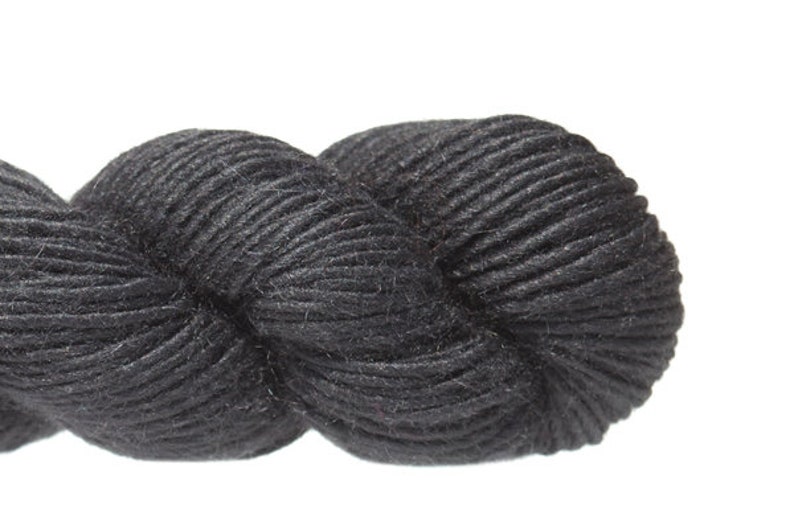 Puede incluir: Un ovillo de hilo negro, un material suave y esponjoso para tejer o hacer ganchillo.