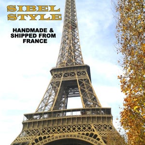 Puede incluir: La Torre Eiffel en Par&iacute;s, Francia, con una estructura de celos&iacute;a de hierro marr&oacute;n contra un cielo azul claro. El texto superpuesto dice SIBEL STYLE HANDMADE & SHIPPED FROM FRANCE en letras amarillas y negras. &Aacute;rboles oto&ntilde;ales a la derecha.