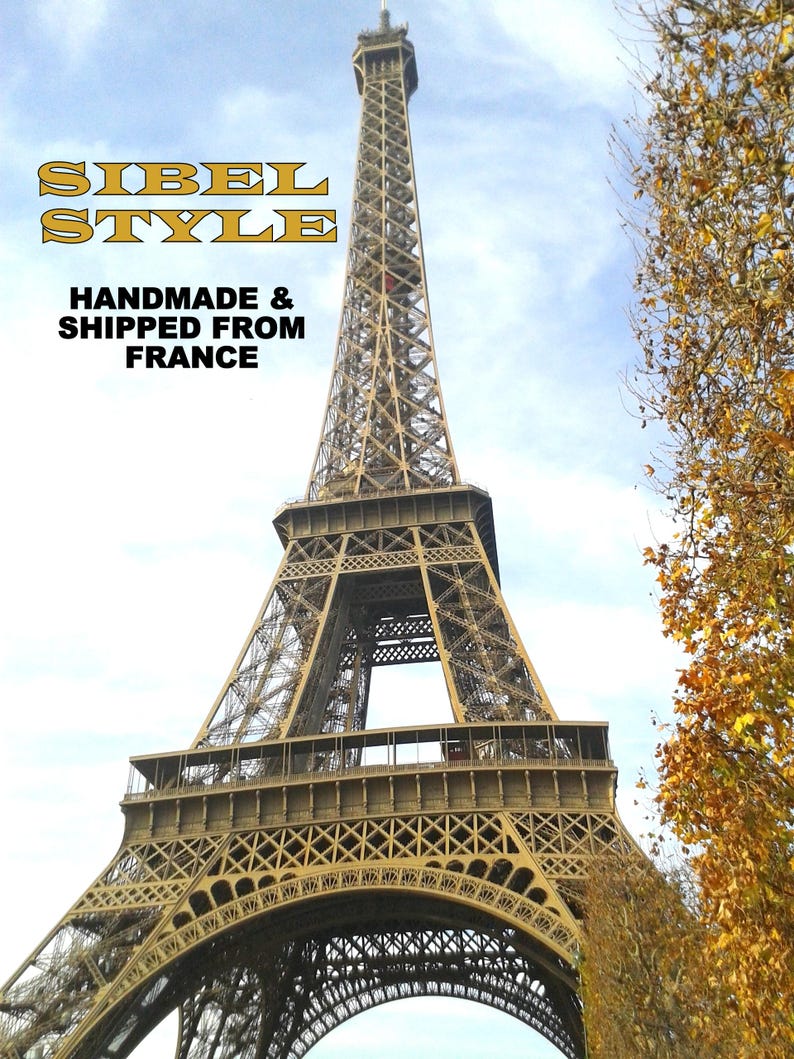 Puede incluir: La Torre Eiffel en Par&iacute;s, Francia, con una estructura de celos&iacute;a de hierro marr&oacute;n contra un cielo azul claro. El texto superpuesto dice SIBEL STYLE HANDMADE & SHIPPED FROM FRANCE en letras amarillas y negras. &Aacute;rboles oto&ntilde;ales a la derecha.