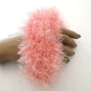 Puede incluir: Un coletero de color rosa claro, esponjoso y hecho de hilo texturizado y desgre&ntilde;ado con sutiles fibras iridiscentes entrelazadas. El accesorio presenta un aspecto suave y voluminoso e incluye el texto Sibel Style impreso en negro a la izquierda.